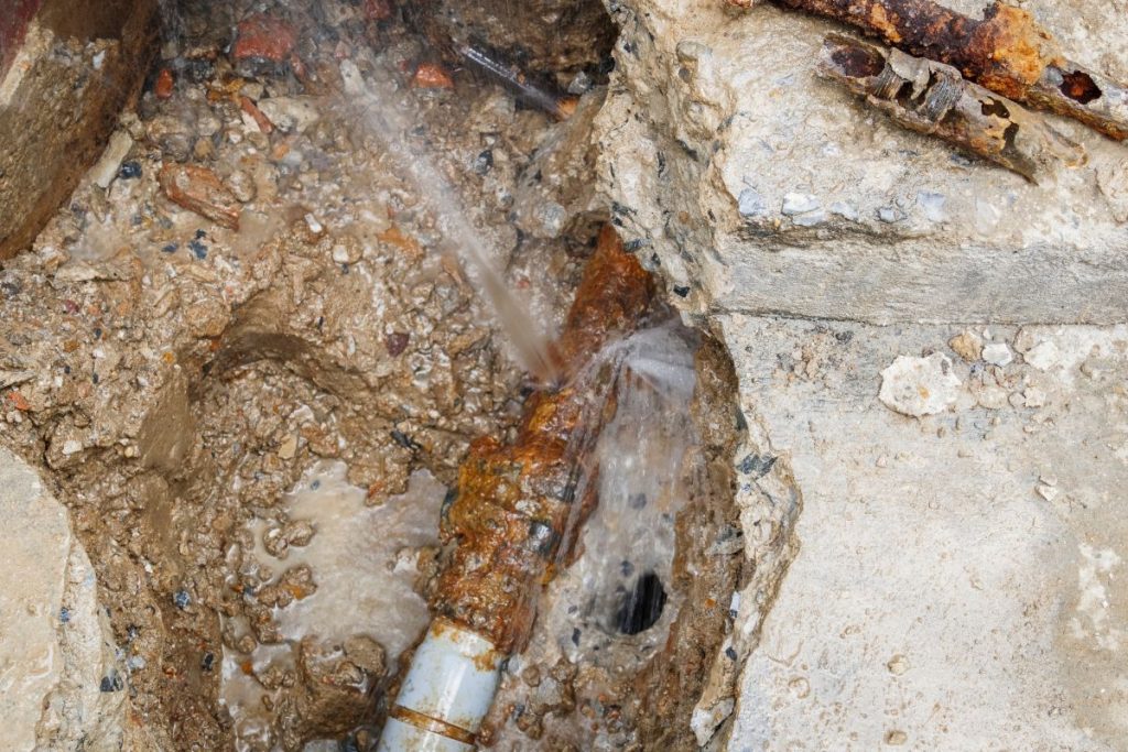a burst and heavily corroded underground pipe leaking water into surrounding mud and broken concrete